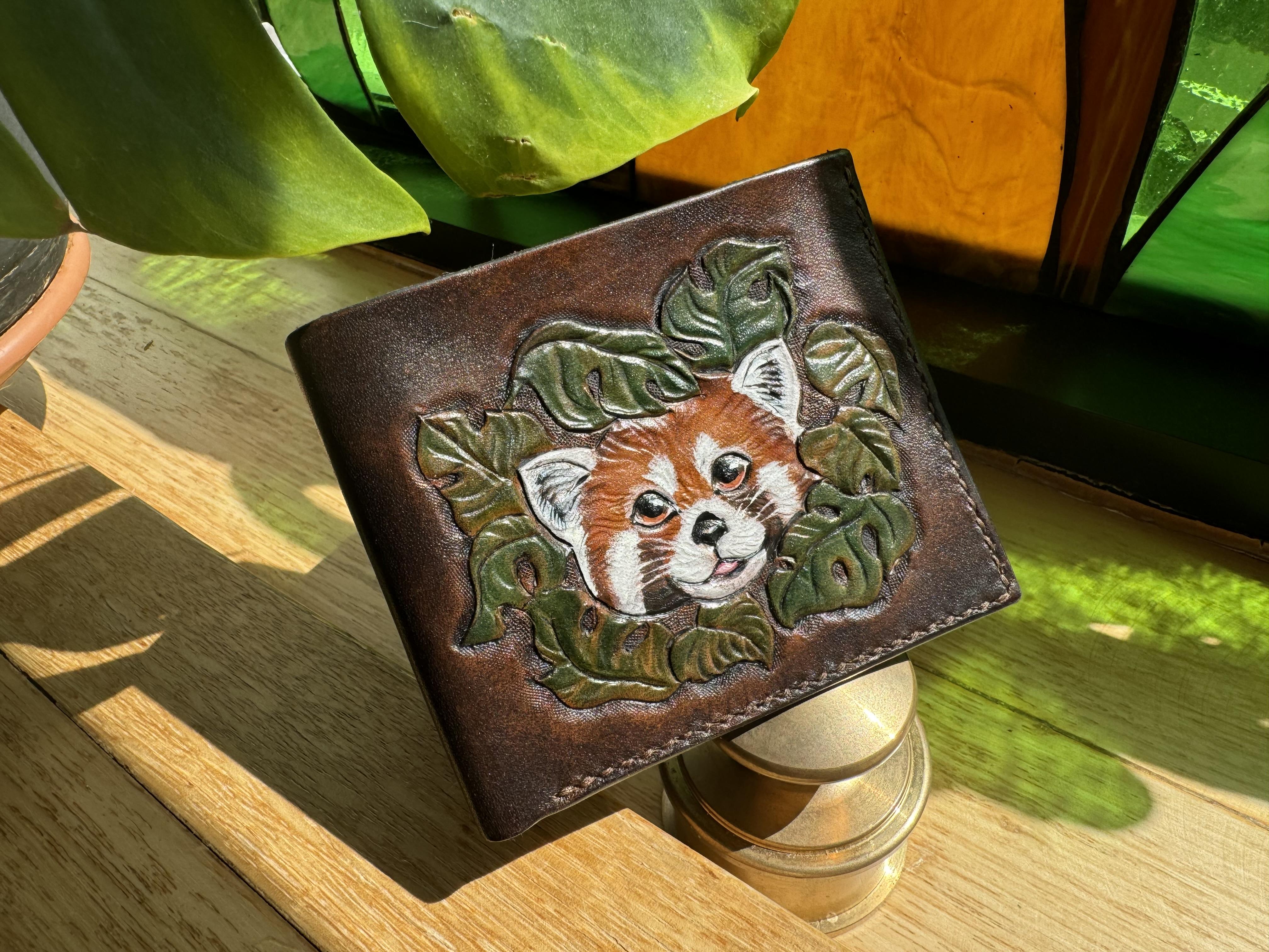 A custom wallet featuring a Red Panda emerging through a forest of Monstera leaves. It was carved on premium Hermann Oak tooling leather and dyed to match the lustrous Italian leather interior.