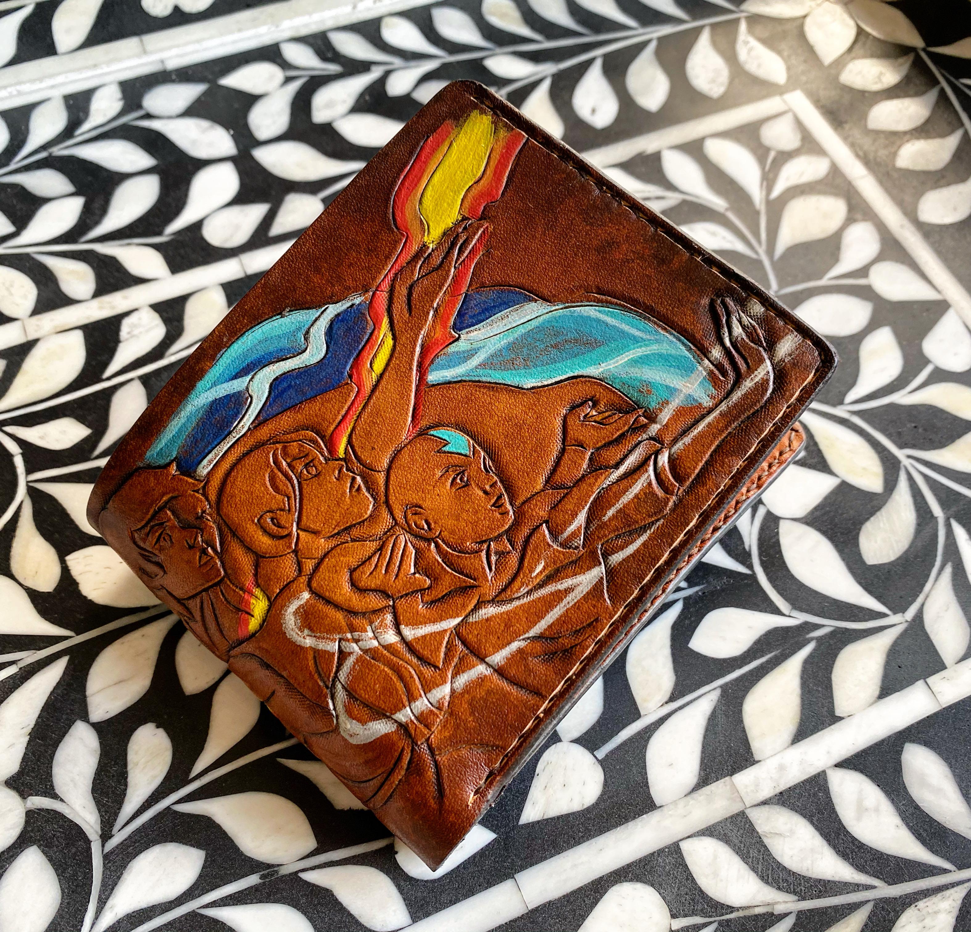 A detailed wallet carved on the exterior, featuring all of the main characters from Avatar: The Last Airbender. The elements were highlighted with vibrant leather paints, on a gradient toned rustic background of dark tan.